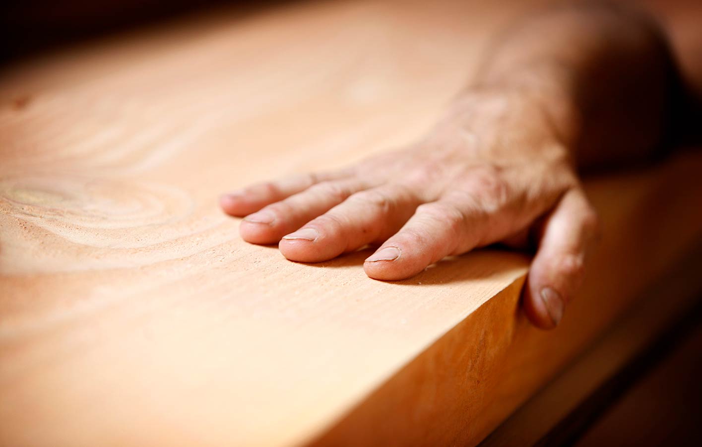 Bauen mit Holz - Holzprodukte mit allen Sinnen genießen Nahaufnahme ein Mann legt seine Hand auf ein Holzbrett